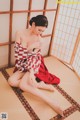 A woman in a red and white kimono sitting on a tatami mat.