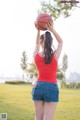 A woman in a red shirt and denim shorts holding a basketball.