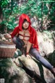 A woman in a red hooded outfit sitting on a rock with a basket.