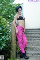 A woman in a black bra top and pink pants posing for a picture.